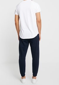 Vit t-shirt med kort ärm och rundad nederkant, ihop med mörkblå joggers med elastiska muddar och vita slip-on skor.