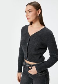 Grijze cropped cardigan met een geribbelde textuur, v-hals, knoopsluitingen en lange mouwen, gecombineerd met hooggetailleerde zwarte jeans.