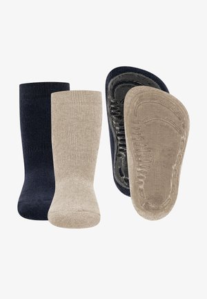 Dwie pary skarpet, jedna granatowa, a druga beżowa, obie z antypoślizgowymi gumowymi gripsami na podeszwach, uporządkowane obok siebie.