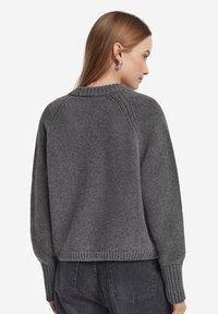 Maglione grigio lavorato a maglia con scollo a girocollo, maniche raglan e polsini e orlo a coste. La trama è morbida e leggermente ampia.