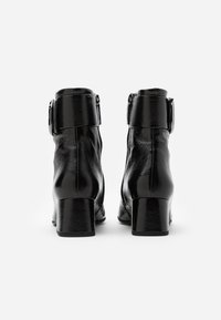 Botas de tobillo de cuero negro con acabado brillante, que presentan un grueso tacón en bloque y un detalle de hebilla metálica en el tobillo. Textura suave.