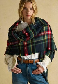 Villane ruuduline rätik tumerohelises, punases ja kollases, mille servad on narmendunud. Kanditud valge pluusi kohal ja kombineeritud kõrge vöökohaga siniste teksapükstega.