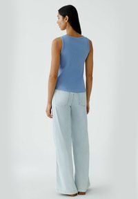 Blue ribbed tank top with round neck and sleeveless design, paired with light blue wide-leg jeans and brown wooden platform shoes.