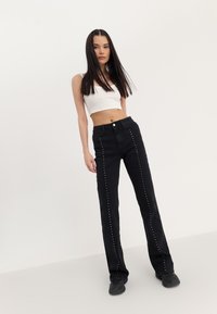 Svarte denimbukser med rett ben-design, med kontrasterende sølvspiker langs sømmene. Kombinert med en hvit kort tanktop.