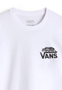 Bílé bavlněné tričko s kulatým výstřihem, které má černé logo Vans a grafiku tygra na levé části hrudi. Design v klasickém střihu.