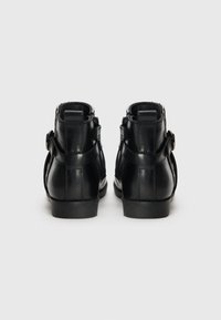 Bottines en cuir noir avec une finition lisse, semelle plate en caoutchouc et détails de courroie sur le côté. L'arrière est doté d'une languette pour un enfilage facile.