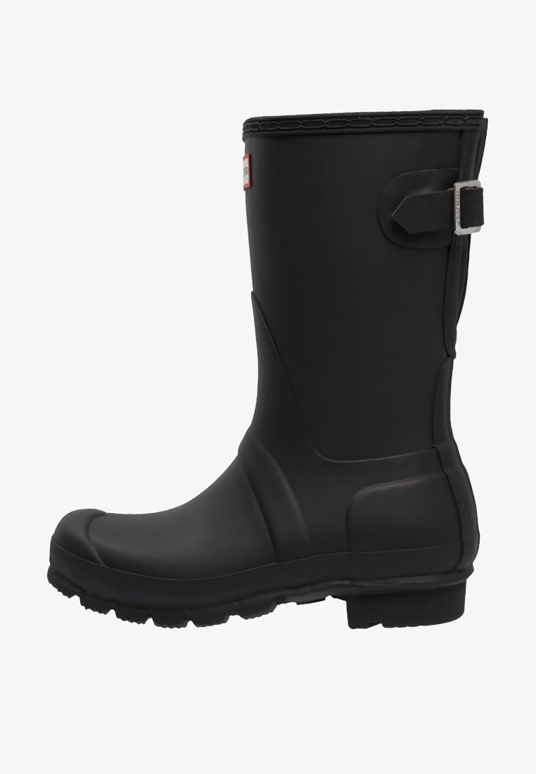Bota de lluvia de caucho negro con una superficie texturada, puntera redonda y un acento de correa en el lateral. Presenta una suela plana duradera para mayor tracción.