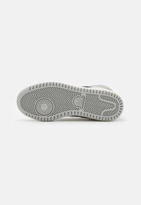 White sneaker sole with a textured gray rubber material. Features a zigzag pattern, circular logo, and a smooth round accent in the center.
