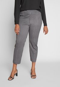 Pantaloni a quadri in misto poliestere bianco e nero, con gamba affusolata e lunghezza alla caviglia, abbinati a sandali neri con cinturino.