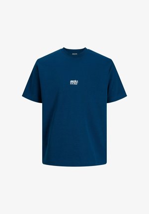 Chłopiec w niebieskiej koszulce z krótkim rękawem, czarnych szortach cargo, białych skarpetkach i czarnych trampkach stoi i patrzy na bok.