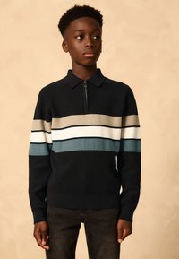 Jersey de punto con cuello de cremallera, con franjas horizontales en azul marino, beige, blanco y teal. Textura suave y diseño ajustado.