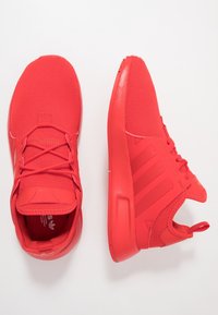 Klarröda sportskor med nätöverdrag, snören och tre ränder på sidan, sedda uppifrån och från sidan på en vit bakgrund.