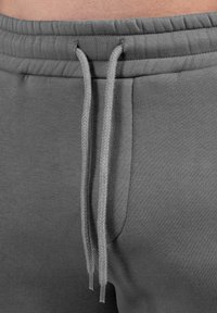 Pantalones deportivos grises con cintura ajustable de cordón, textura suave, bolsillo lateral y detalles de costura a lo largo de los bordes.