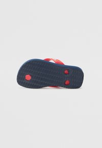 Red flip-flop with a textured navy blue sole. Features two red straps across the top and circular grip patterns on the bottom.