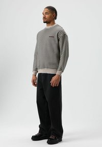 Gestreepte sweatshirt in beige en zwart, met een ronde halslijn en geribde manchetten, gecombineerd met losse zwarte jeans en zwarte schoenen.