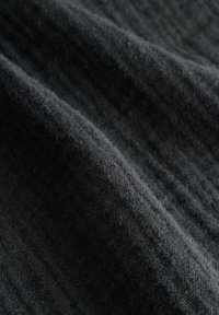 Textúrovaná čierna tkanina s jemným, trochu chmýřivým povrchom. Obsahuje jemné, lineárne vzory, ktoré vytvárajú hĺbku a vizuálny záujem.