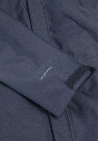 Mörkblå väderbeständig jackärm med strukturerad tyg, kardborrestängning och "HYDROSHELL"-logotyp.