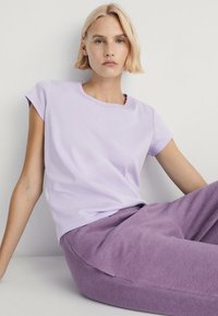 Lys lilla kortærmet t-shirt med rund halsudskæring og afslappet pasform, parret med matchende lilla sweatpants. Blødt stof og glat tekstur.