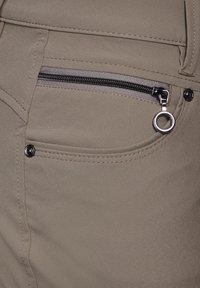 Beige Hosen mit einer Reißverschlusstasche, die einen silbernen Reißverschluss und einen Ringzug hat. Glatte Textur und detaillierte Nähte um die Taschen.