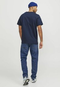 T-shirt di cotone blu navy a maniche corte, abbinata a jeans in denim a vestibilità ampia. L'outfit è completato da sneakers bianche e blu navy.