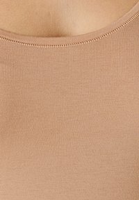 Beige tank top featuring a ribbed texture, round neckline, and smooth seams. The fabric appears soft and form-fitting.