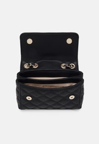 Sort quiltet læderpung med guldtonede trykknapper og kædestrop, åben for at vise beige indvendig foring med "GUESS" logo.