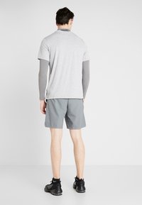 Grå T-shirt med kort ärm i kombination med grå träningsshorts. T-shirten har rund hals och har en mörk etikett på baksidan.