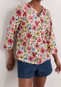 Blusa a bottoni floreale bianca con fiori rosa, rossi e gialli. Presenta maniche a tre quarti e scollo a V. Tessuto leggero e testurizzato.