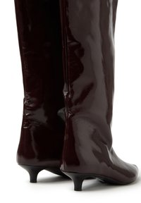 Botas hasta la rodilla burdeos brillantes con forma ajustada y punta afilada, que cuentan con un tacón bajo tipo kitten y una superficie de textura suave.