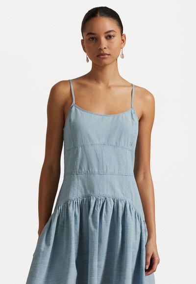 Robe en jean bleu clair avec des bretelles fines, un corsage ajusté et une jupe froncée. Le matériau semble doux avec des détails de couture visibles.