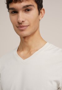 Gai beigā V veida t-krekls izgatavots no mīkstas auduma, ar īsām piedurknēm un vienkāršu, gludu tekstūru bez rakstiem vai rotājumiem.