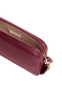 Portafoglio in pelle bordeaux con zip dorata, caratterizzato da una texture liscia e una piccola tasca interna. Design piegato, dimensioni compatte, minimal hardware.
