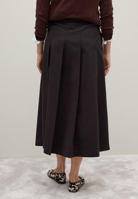 Gonna midi a pieghe nera con una texture liscia, dettaglio in vita, abbinata a ballerine con stampa animale. Design minimalista, vista posteriore mostrata.