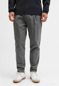 Graue Hosen mit entspannter Passform, gefertigt aus weichem Material. Kombiniert mit weißen Sneakers mit beigen Akzenten. Einfaches Design ohne zusätzliche Muster.