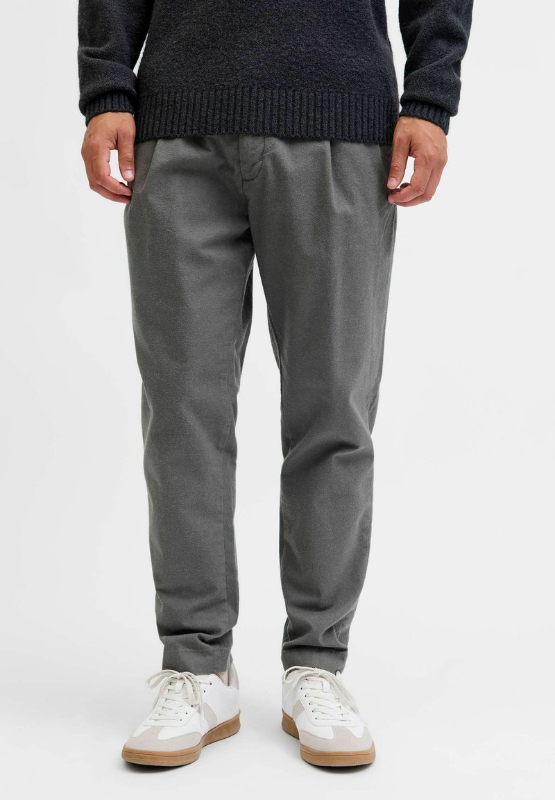 Graue Hosen mit entspannter Passform, gefertigt aus weichem Material. Kombiniert mit weißen Sneakers mit beigen Akzenten. Einfaches Design ohne zusätzliche Muster.