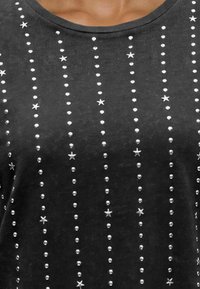 Gros plan d'une chemise sombre avec des rangées verticales de petits clous ronds et des embellissements métalliques en forme d’étoile sur le devant.