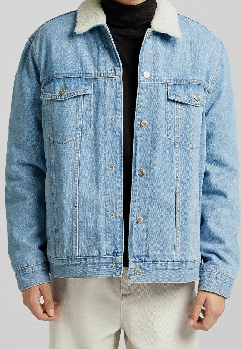 Giubbotto di jeans blu chiaro con colletto bianco peloso, chiusura con bottoni, due tasche anteriori sul petto e un fit rilassato. Tessuto testurizzato.