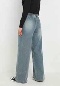 Pantaloni in denim azzurro chiaro a gamba larga con vita elastica, dotati di una tasca posteriore e orlo sfilacciato. Abbinati a sneakers nere.