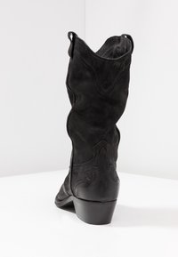 Czarne zamszowe kowbojskie buty z dekoracyjnym haftem i pętelkami do zakupu, ustawione w kącie, pokazując tył i bok na białej powierzchni i jasnym tle.