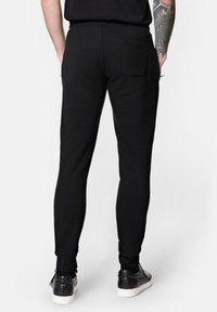 Czarne spodnie dresowe o dopasowanym kroju, z prążkowanymi mankietami i tylną kieszenią. Połączone z czarnymi teksturowanymi sneakersami. Gładka struktura materiału.