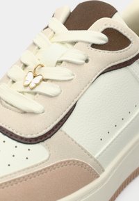 Αθλητικό παπούτσι με συνδυασμό ανοιχτού πράσινου, ταμπά και καφέ δέρματος με υφή. Χρυσό μενταγιόν πεταλούδας στο σημείο των κορδονιών.