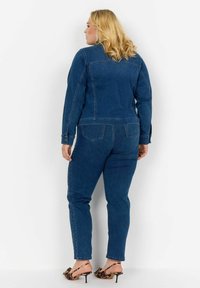 Zila džinsa jaka un atbilstošas bikses ar pieguļošu siluetu. Tekstūrēta auduma ar redzamām šuvēm. Nēsāta ar leoparda raksta papēžu sandālēm.