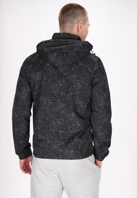 Sort jakke med bladmønster, der har hætte og elastiske manchetter. Designet har en mat finish, der skaber et slankt, struktureret udseende.