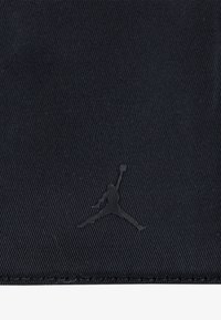 Schwarzer Stoff mit einer gerippten Struktur, versehen mit einem erhabenen schwarzen Jumpman-Logo. Schlichtes Design ohne zusätzliche Muster oder Akzente.
