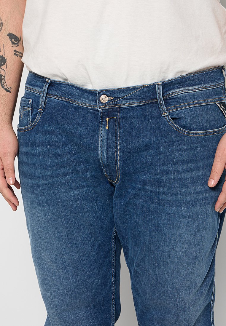 Denim jeans in donkerblauw, met een rechte pasvorm, vijf-pocket ontwerp en contrasterende gele stiksel. Knop- en ritssluiting zichtbaar.