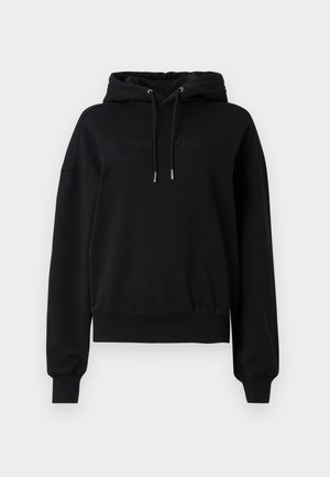 Črna kapuca iz mehkega blaga, z vrvico za zategovanje, ribastimi manšetami in diskretnim reliefnim logotipom spredaj.