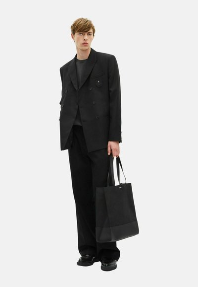 Blazer negro ajustado de doble botonadura con bolsillos de solapa, combinado con pantalones de pierna ancha a juego y un bolso tote negro, llevado con zapatos negros.