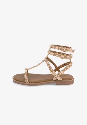 Sandalia plana color camello con múltiples tiras, cuero sintético texturizado, hebillas doradas y suela acolchada. Presenta un diseño minimalista y tachuelas en la suela.