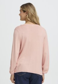 Pull rose pâle à manches longues avec un col rond. Présente des manches légèrement bouffantes et une coupe décontractée, fabriqué en maille douce.