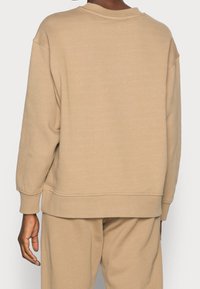 Felpa beige, oversize, con maniche lunghe, scollo rotondo e polsini a coste. Texture morbida e liscia con un design semplice e pulito.